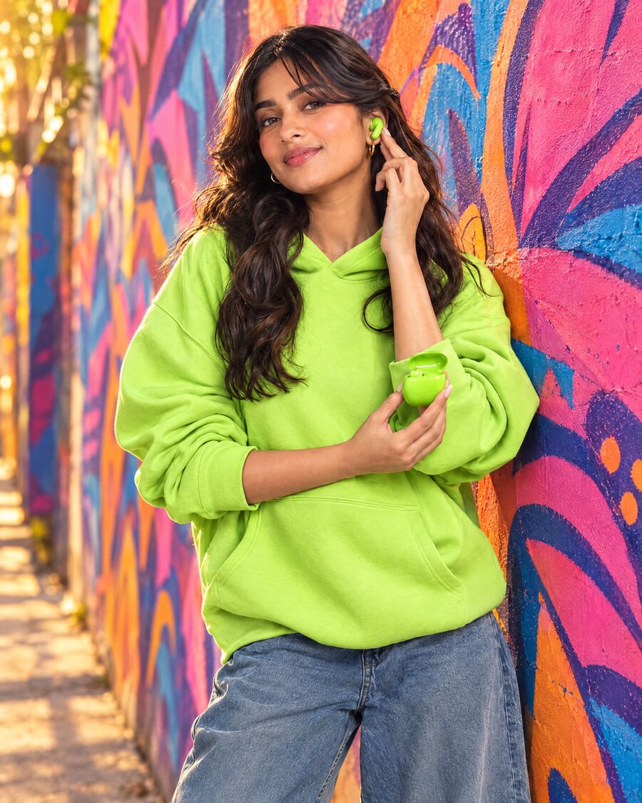 Model in a cyber lime hoodie with matching lime earbuds against a graffiti wall